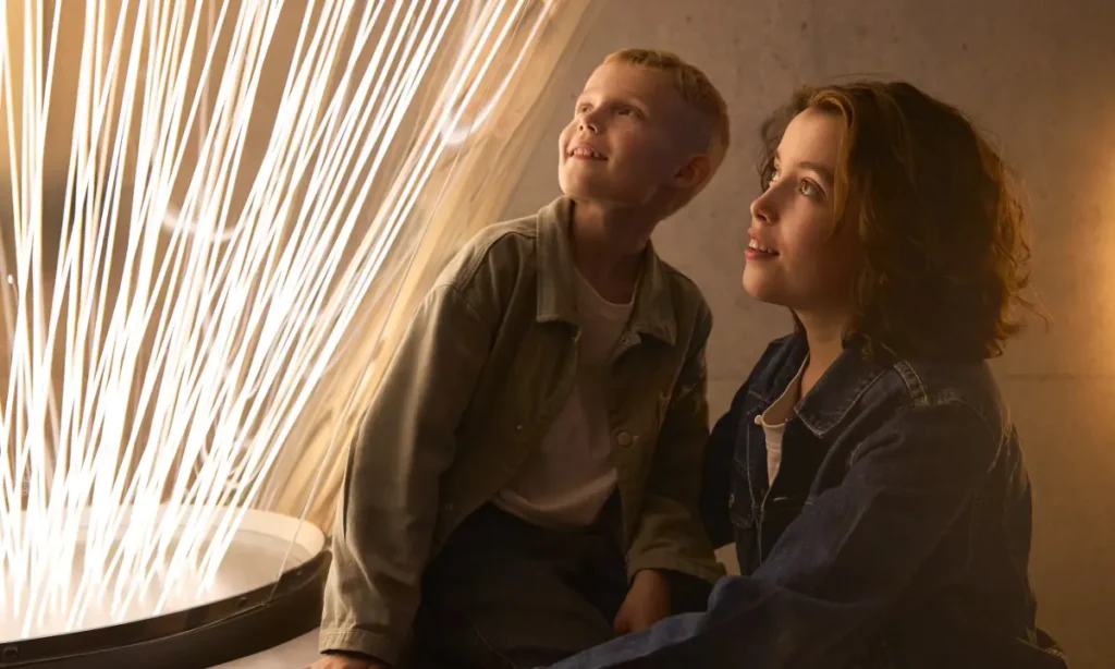 To børn sidder ved en interaktiv skærm på Planetarium og kigger op på et spektakulært lysmønster, der illustrerer forbindelsen mellem Jorden og rummet i den nye udstilling Rummet T/R.